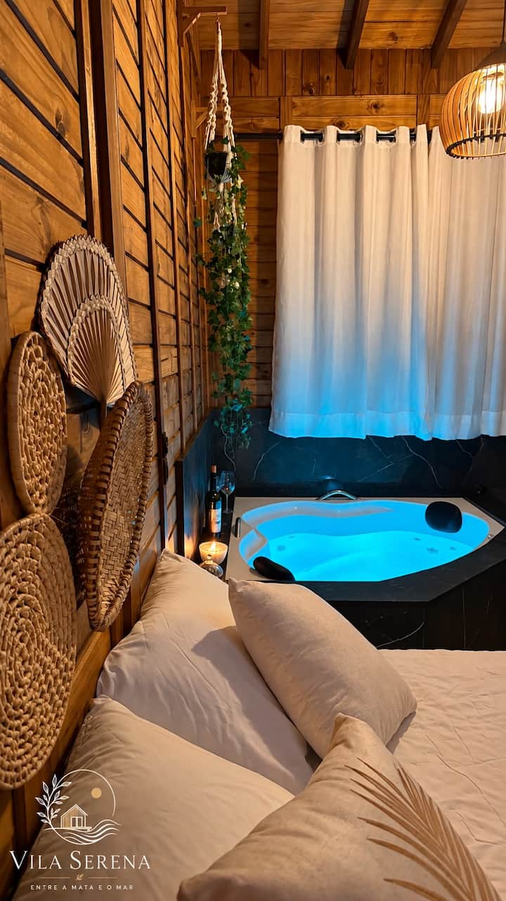 Estúdio de madeira à noite, com a banheira acesa em azul ao lado da cama de casal