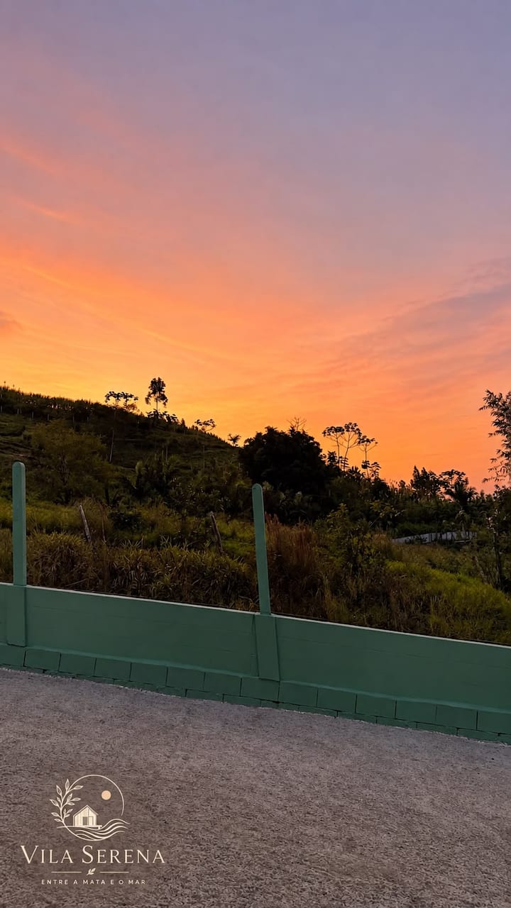 Pôr do sol laranja sobre os morros, visto da entrada da Vila